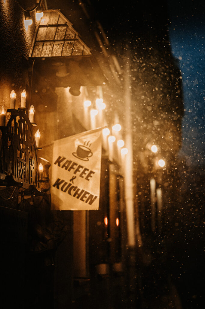 Schneegestöber im Gegenlicht an einem erzgebirgischen Cafe mit Schwibbogen und Lichterglanz am Eingang 